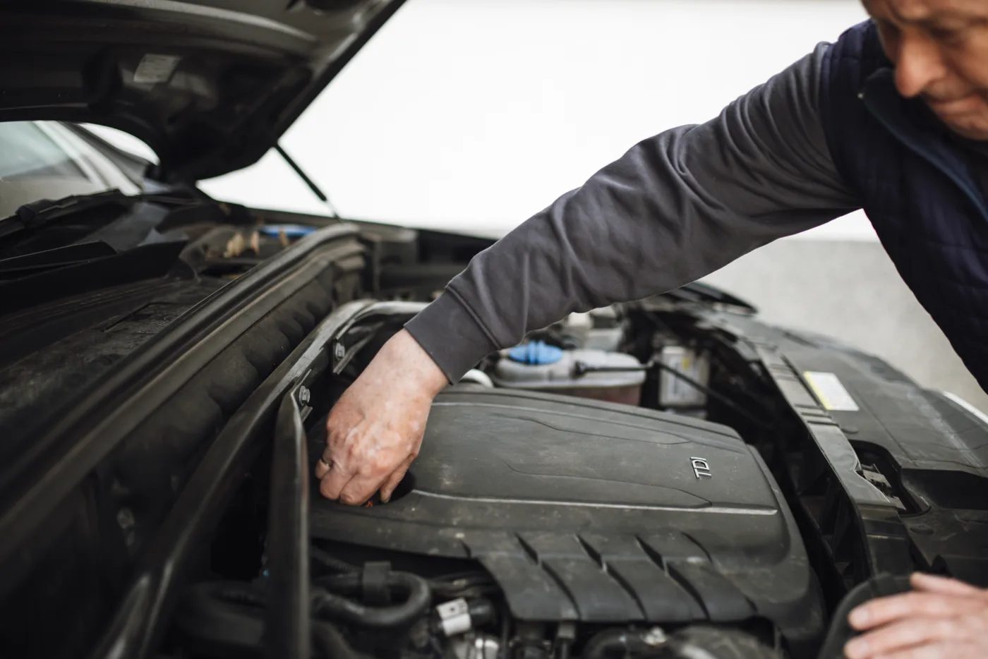A mechanic leans over an open engine bay to inspect components in a workshop.